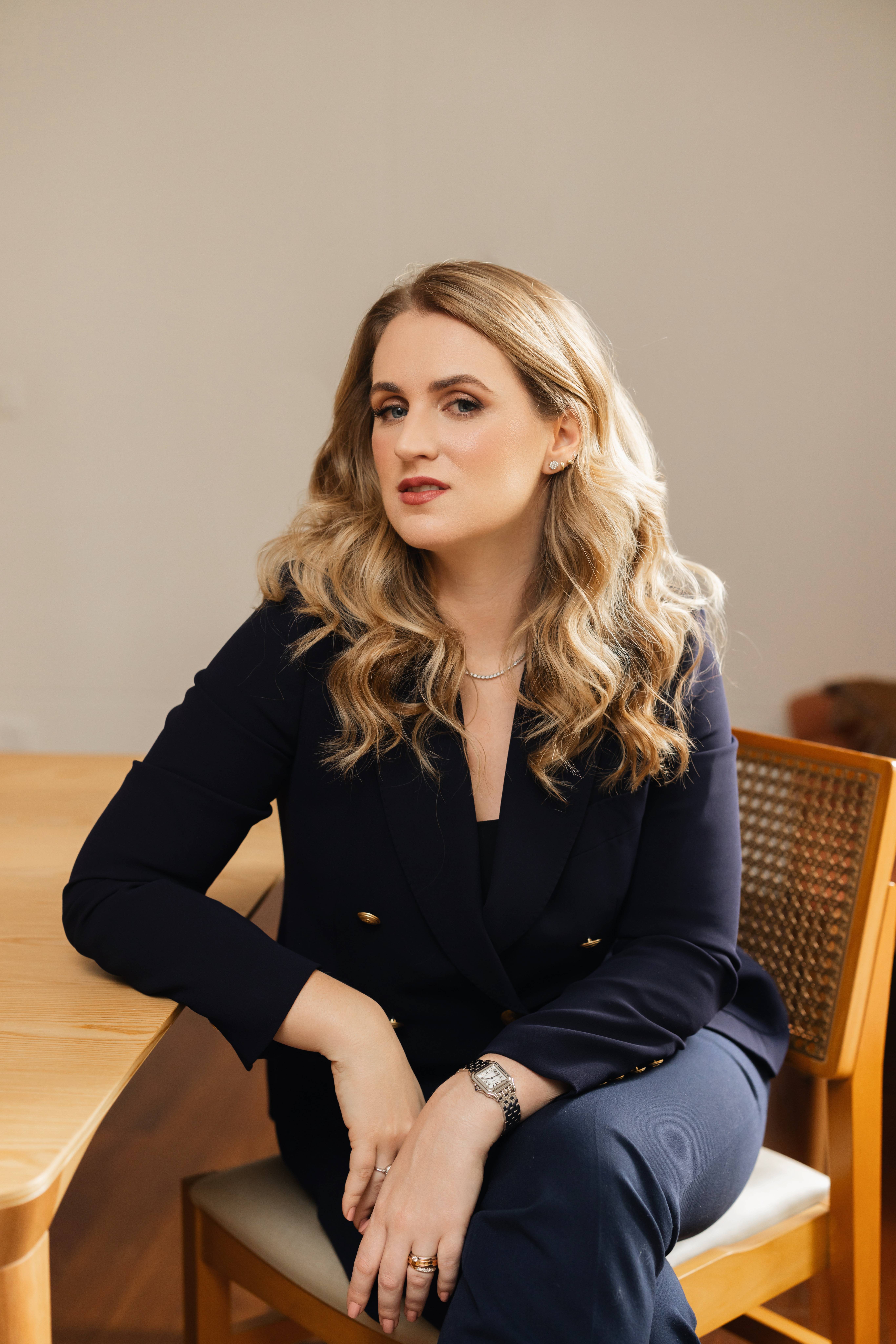 Anelize Caminha, de blazer azul-marinho, sentada à mesa